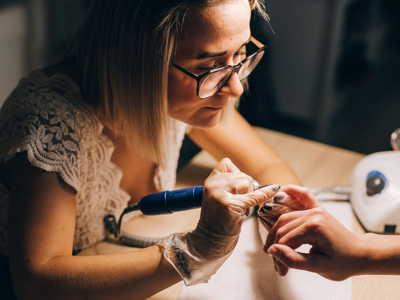 Nail technician using an electric nail drill on a client's nails