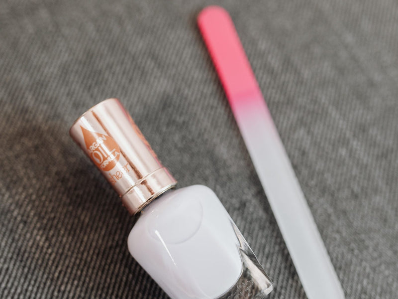 White nail polish bottle and a glass nail file on grey fabric