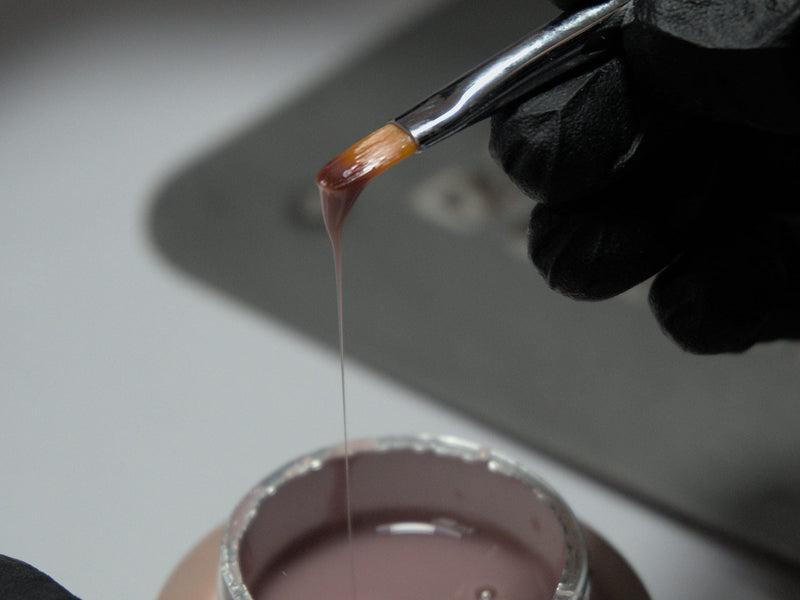 Nail brush loaded with gel polish above an open gel pot